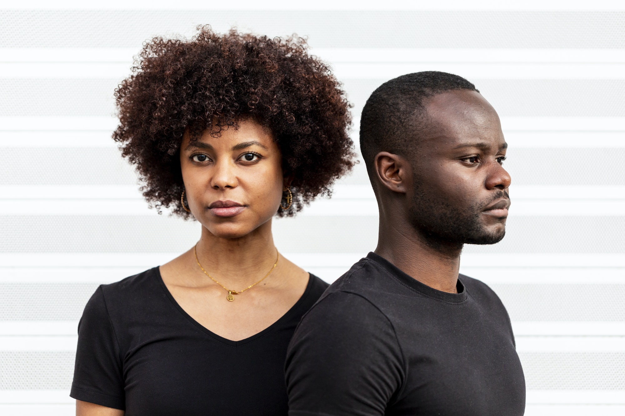 Serious black couple near striped wall in daytime